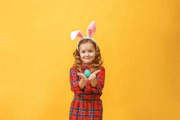 Cheerful little kid girl with bunny ears with an easter egg on a colored background.