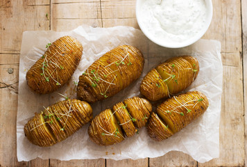 Hasselback potatoes served with cheese and sour cream sauce on a wooden table. Rustic style.