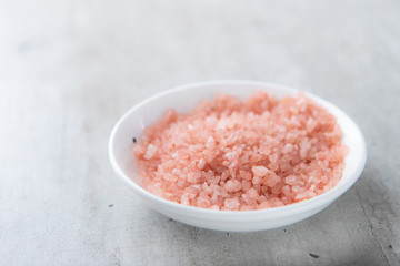 Himalayan pink salt in a white bowl on a gray background. Close up.