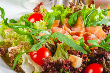 Salad with salmon, cherry tomatoes, croutons and lettuce on white plate. Close up