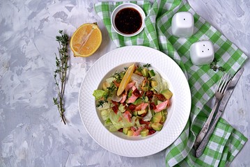 Green salad with avocado, baked salmon and dried tomatoes in a white plate on a gray concrete background. Top view.