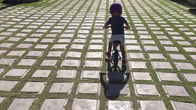 The boy rides a bike on the road of tiles in the form of squares and grass.