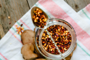 Ground dried chili pepper spilled from glass can  and rustic spoon. Crushed chillies. Top view.