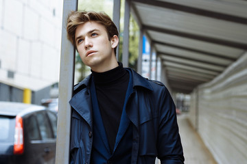 thin, attractive young man standing on the street, leaning on the frame, sad, posing.