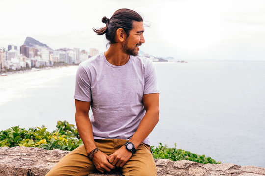 Smiling Mature Man Looking At Sea While Sitting On Retaining Wall In City