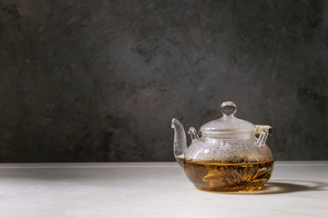 Hot green tea in transparent glass teapot standing on white marble table.