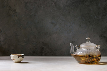 Hot green tea in traditional chinese clay ceramic cup and glass teapot standing on white marble table.