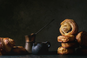 Variety of homemade puff pastry buns cinnamon rolls and croissant served with vintage coffee pot on wooden table. Dark still life. Copy space - Powered by Adobe