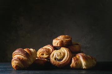 Fotobehang Variety of homemade puff pastry buns cinnamon rolls and croissant on wooden table. Dark still life. Copy space © Natasha Breen