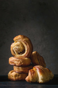 Variety of homemade puff pastry buns cinnamon rolls and croissant on wooden table. Dark still life. Copy space