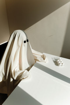 Person In Ghost Costume Sitting By Table At Home