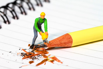 Conceptual diorama image of a miniature figure sharpening a pencil on a note book