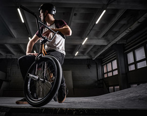 Professional BMX rider in protective helmet sitting on his bicycle in a skatepark indoors