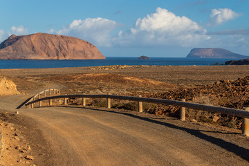 La Graciosa Island, Canary, Spain landscape with a typical unpaved sand road leading to the sea through a serene Mars like volcanic landscape. 
