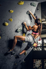 A young woman wearing sportswear practicing rock-climbing on a wall indoors