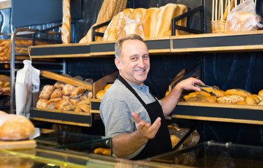 Smiling mature man baker offering fresh baguettes