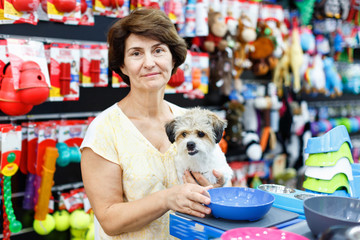 Mature woman choosing accessories for her puppy in pet supplies store