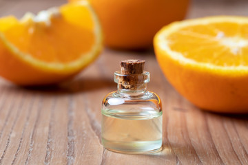 A bottle of orange essential oil with fresh oranges in the background