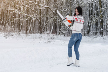 Woman in a sweater and jeans holds a chainsaw in her hands in the woods. Deforestation, sawing, lumberjack and forestry equipment.