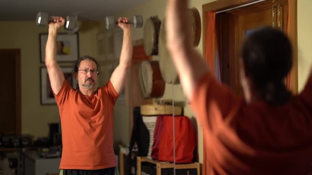 Mature Man Doing Squat Thrusters With Dumbbells In A Home Exercise Area.