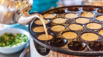 Khanom Khrok (coconut rice pancake), Traditional Thai Pudding Pancake Dessert, prepared by mixing rice flour, sugar, and coconut milk to form dough cooked in heating mantle (hot indented frying pan) - obrazy, fototapety, plakaty