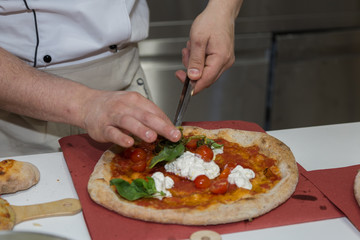 Pizza Maker who Prepares a Delicious Pizza with Cheese,  Cherry Tomatoes and Basil