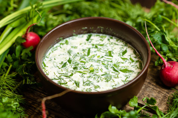 Okroshka in a clay plate on the background of parsley and dill, Russian cold soup