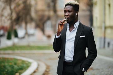 Young handsome african business man Smoke e-cigarette on the city sunny street. Vape gadget.