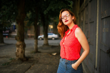 Attractive redhaired woman in eyeglasses, wear on red blouse and jeans skirt posing.