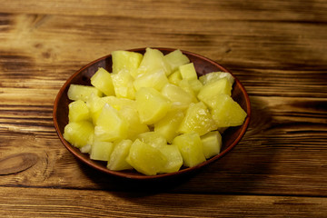 Canned pineapple pieces in ceramic plate on wooden table