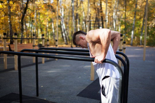 Fit man doing triceps dips on parallel bars at park exercising outdoors