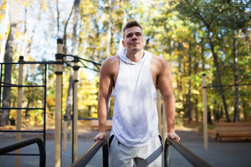 Fit man doing triceps dips on parallel bars at park exercising outdoors