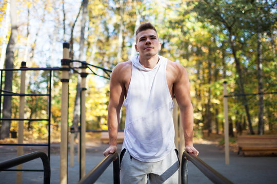 Fit man doing triceps dips on parallel bars at park exercising outdoors