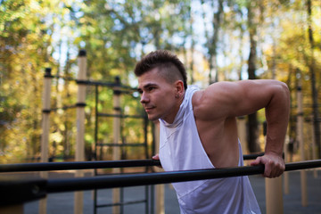 Fit man doing triceps dips on parallel bars at park exercising outdoors