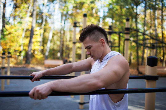 Fit man doing triceps dips on parallel bars at park exercising outdoors