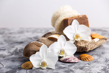 Naklejka na ściany i meble White orchid flowers next to sea stones and shells on a gray background - spa treatments and relaxation concept