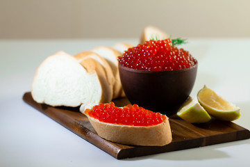 red caviar in a ceramic dish on a wooden platform on a white background
