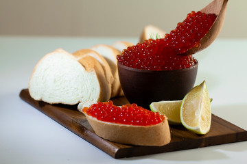 red caviar in a ceramic dish on a wooden platform on a white background