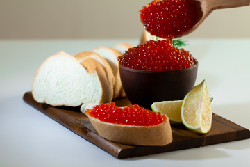 red caviar in a ceramic dish on a wooden platform on a white background