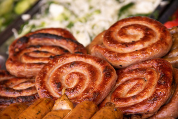 Roasted spiral sausages on a plate of greenery and vegetables in the background