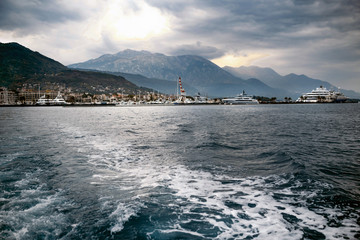 Fototapeta premium White yacht crosses sea leaving mountains with fog behind it