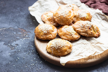Fresh meat mini pies on a paper on a old dark brown background, rustic style. Fresh baked pasties filled with meat (chicken or turkey). Copy space.