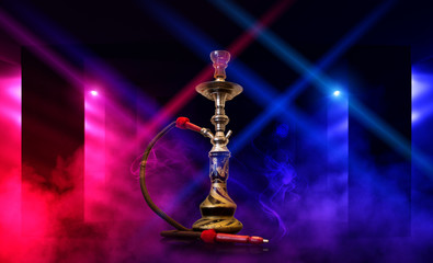 Smoking hookah on the background of an empty room. Multicolored neon light. Searchlight, laser blue and pink rays, smoke.