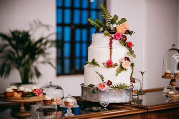Delicious white wedding cake decorated with flowers stands in the middle of dinner table