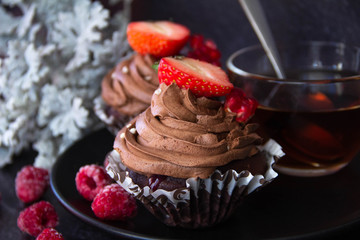 Chocolate cupcakes with berries on black plate.