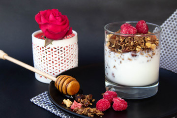 Granola with yoghurt and berries in glass on black plate.