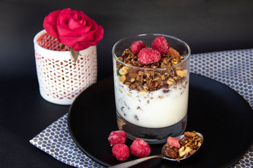 Granola with yoghurt and berries in glass on black plate.
