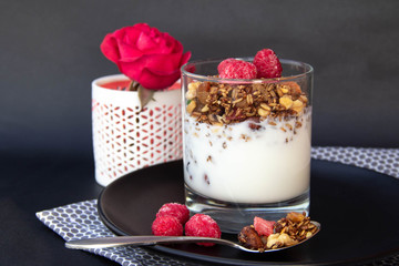 Granola with yoghurt and berries in glass on black plate.