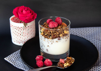Granola with yoghurt and berries in glass on black plate.