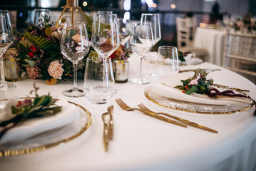 Wedding dinner table setting. White clothes with golden decor and flower bouquets in the center